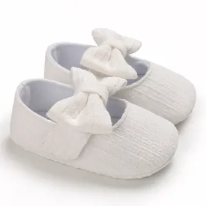 Close-up detail of white baby princess walking shoes featuring a soft ribbed fabric and large bow