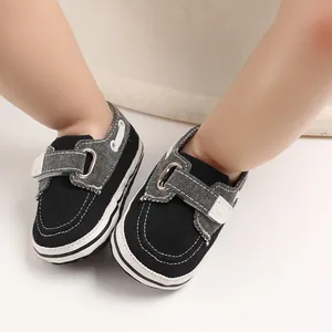 Dettaglio di scarpe da bambino in tela nera con cinturini in velcro denim grigio.