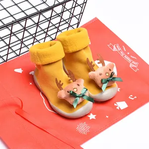 Detalle de zapatos calcetín amarillos para bebé con peluche de reno navideño y lazo verde