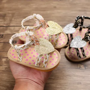 Close-up of baby girl sandals featuring glitter heart decorations and braided straps.
