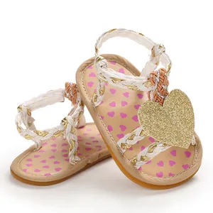 Detail of baby girl sandals with braided straps and a large gold glitter heart ornament.