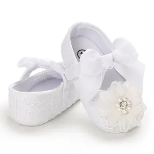 Close-up of white lace infant baby girl shoes with bow and floral pearl detail