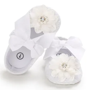 Detailed view of white infant princess shoes featuring lace flowers and large grosgrain bows