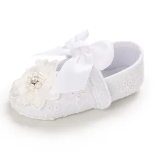 Close-up detail of baby girl white lace princess shoe with large bow and pearl flower