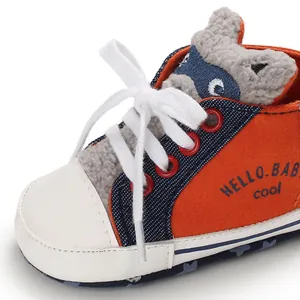 Close-up detail of infant walking shoe featuring a cute raccoon tongue and orange canvas