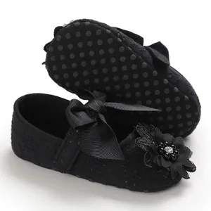 Close-up detail of black infant princess shoes featuring lace texture and floral bow decor
