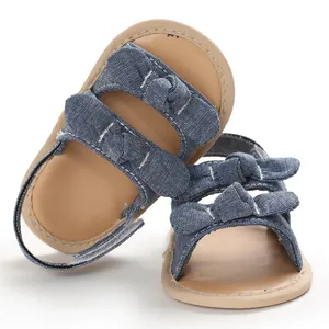 Gros plan sur des sandales bébé en jean bleu avec semelles souples et nœuds déco