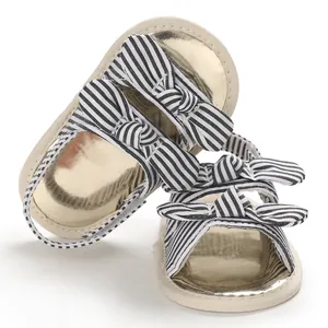 Vue détaillée de sandales pour bébé avec nœuds à rayures noires et blanches et semelles dorées.