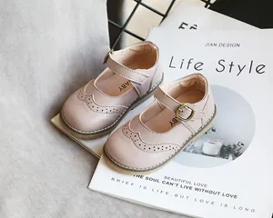 Pink children's Mary Jane leather shoes with brogue detailing on book background