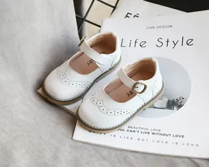 Close-up of white Mary Jane shoes for girls with elegant brogue patterns on a magazine.