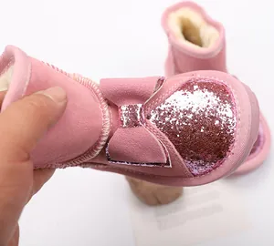 Close-up of pink glittery children's snow boots with bow accent and warm plush lining.