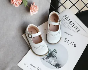 Detailed view of white girl's Mary Jane shoes featuring perforated wingtip design and buckle