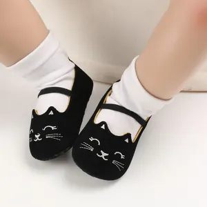 Close-up of black baby walker shoes with embroidered cat face and elastic strap.