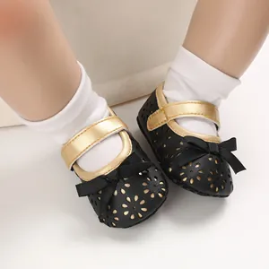 Detail von schwarzen Baby-Prinzessin-Schuhen mit goldenen Riemen und Blumenmuster.