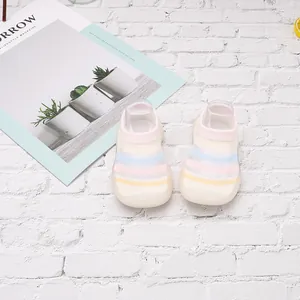 Zapatos tipo calcetín para bebé con rayas de arcoíris sobre fondo de ladrillo blanco