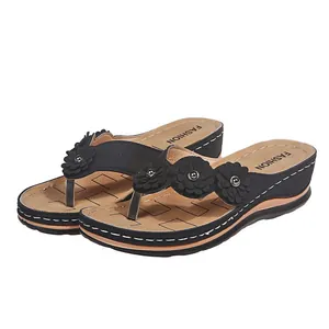 Vista detallada de chanclas con cuña negras y flores con diseño calado láser.