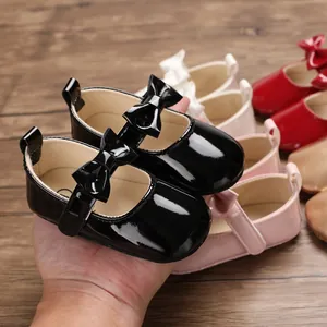 Premium glänzende schwarze PU-Leder Baby-Lauflernschuhe mit Schleife in der Hand.