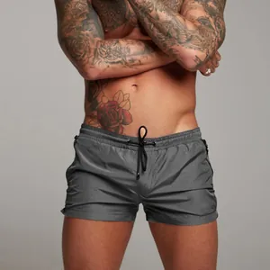 Close-up of men's gray gym shorts with zipper pockets and drawstring on a muscular model.