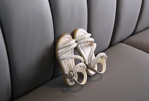 Elegante Mädchensandalen mit Perlenriemen und Metallschnalle auf grauem Sofa