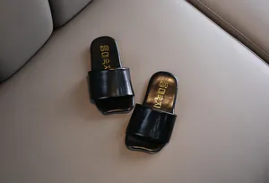 Primer plano de sandalias infantiles de piel sintética negra con texto dorado en relieve