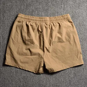 Back view detail of khaki athletic shorts with elastic waistband on grey carpet