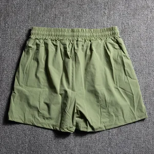 Detail view of olive green men's lightweight athletic shorts on a textured background.