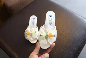 Detailed view of white girl's slipper with elegant gauze bow and colorful beads