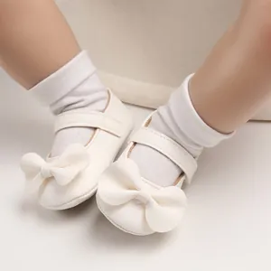 Gros plan de chaussures de marche princesse pour bébé blanches avec un grand nœud.