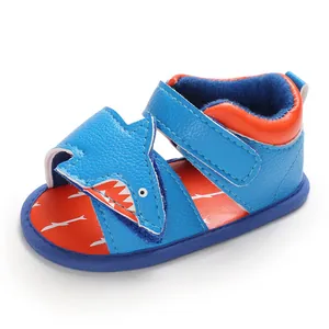Close-up detail of blue cartoon shark themed baby walking sandals with soft orange sole