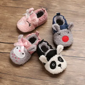 Detalle de zapatos de felpa para bebé con suela blanda y varias caras de dibujos animados.