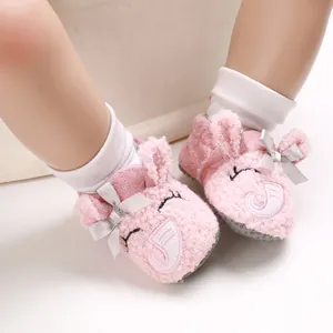 Primer plano de zapatos de bebé de felpa rosa con orejas de conejo y suelas blandas.