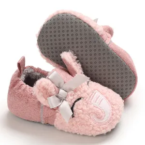 Detalle de zapato de peluche rosa para bebé con orejas de conejo y un lazo gris suave