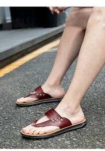 Detailed view of brown leather thong sandals with metal rivets on asphalt ground