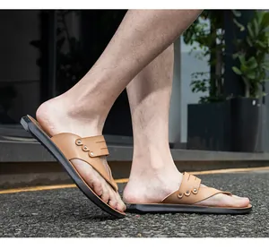 Close-up of stylish brown leather flip-flops with metal studs worn by a model on pavement