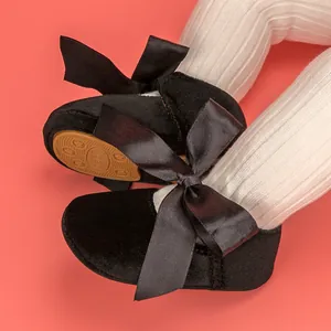 Close-up of black velvet baby shoes featuring elegant satin ribbon bows and soft soles