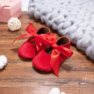 Close-up of red velvet baby princess shoes with elegant large satin bows on wood surface