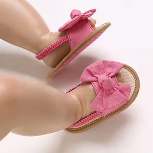 Detalle de sandalias rosas para bebé con lazo grande y suela blanda antideslizante.