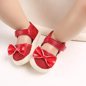 Close-up of red baby walking shoes featuring a large shiny bow and a soft, flat sole