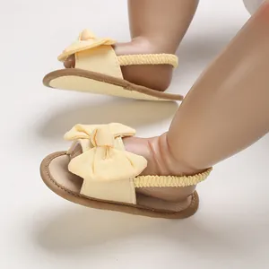 Primer plano sandalias amarillas para bebé con lazo y suela marrón suave verano