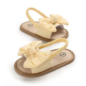 Primer plano de sandalias amarillas para bebés con un gran lazo decorativo.