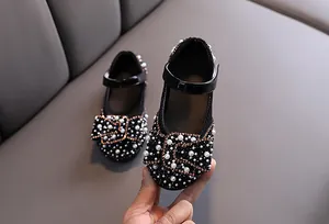 Detailed close-up of girl's black Mary Jane shoes with pearl and rhinestone bow