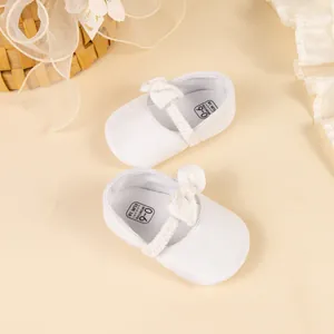 Detailed close-up of soft white plush baby shoes with bow for infants aged 0-6 months