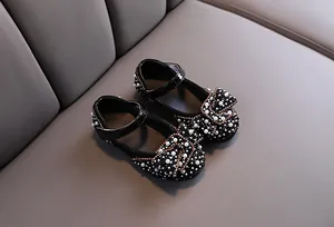 Close-up of black girl's shoes decorated with white pearls, rhinestones and a cute bow