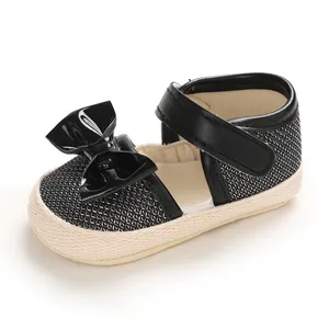 Detail view of black baby walker shoes with a shiny bow and textured white soft sole
