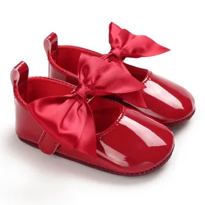 Primer plano de zapatos de bebé en charol rojo brillante con un gran lazo de cinta elegante