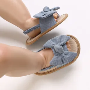 Primer plano de sandalias de bebé en denim azul con lazo grande y suela blanda.