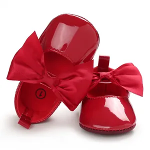 Detalle de zapatos de bebé en charol rojo brillante con un gran lazo decorativo rojo