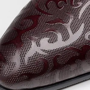 Macro detail view of embossed ornamental scroll pattern on burgundy leather dress shoe.