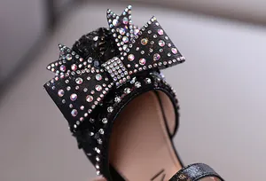 Close-up of sparkling rhinestone bow on girls' black princess leather shoes