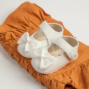 Détail de chaussures princesse blanches pour bébé avec nœuds satinés et bordure dentelle